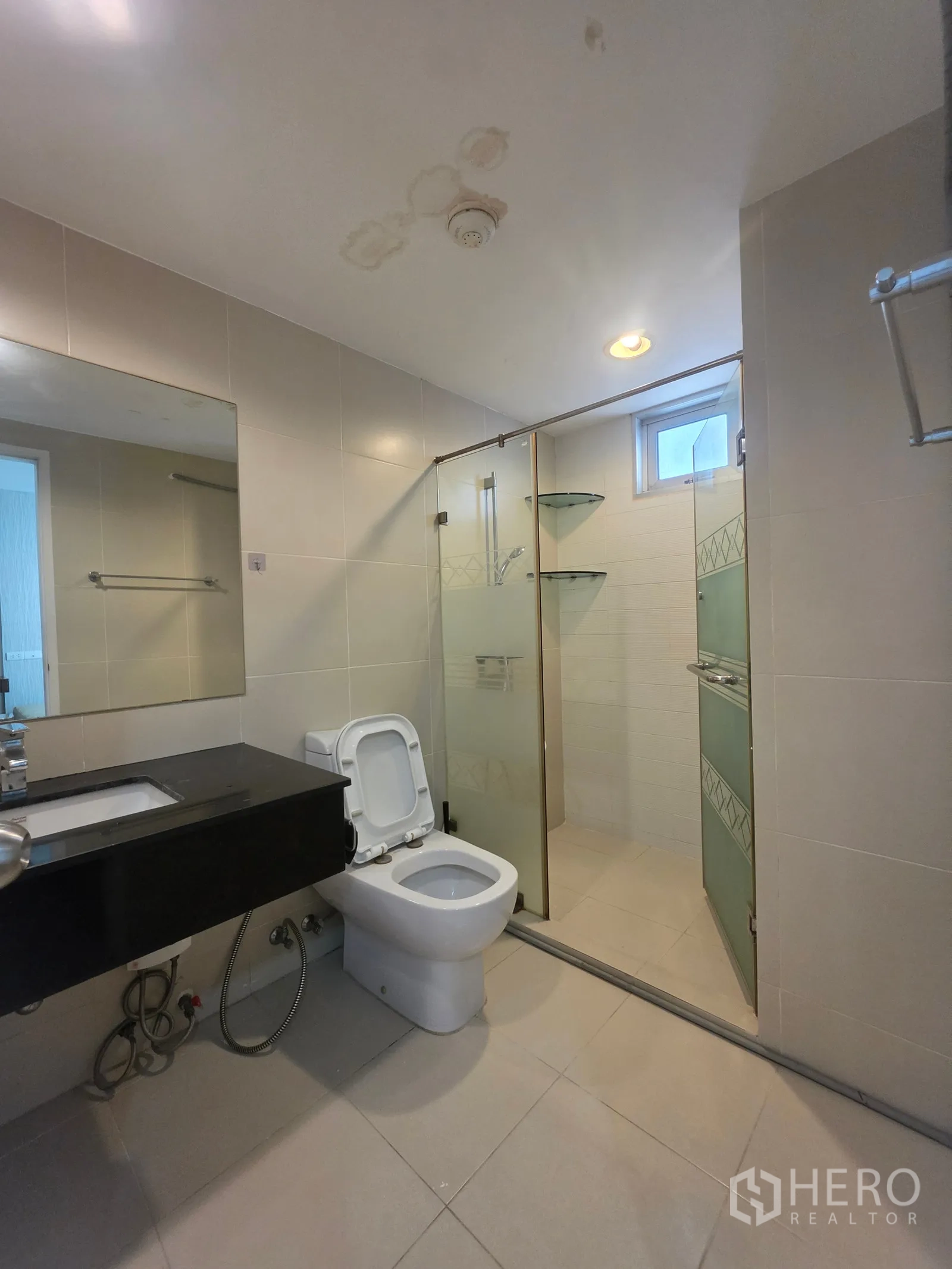 Condominium for rent in Huai Khwang, Bangkok - Bathroom with glass-enclosed shower, large mirror, vanity, and toilet.