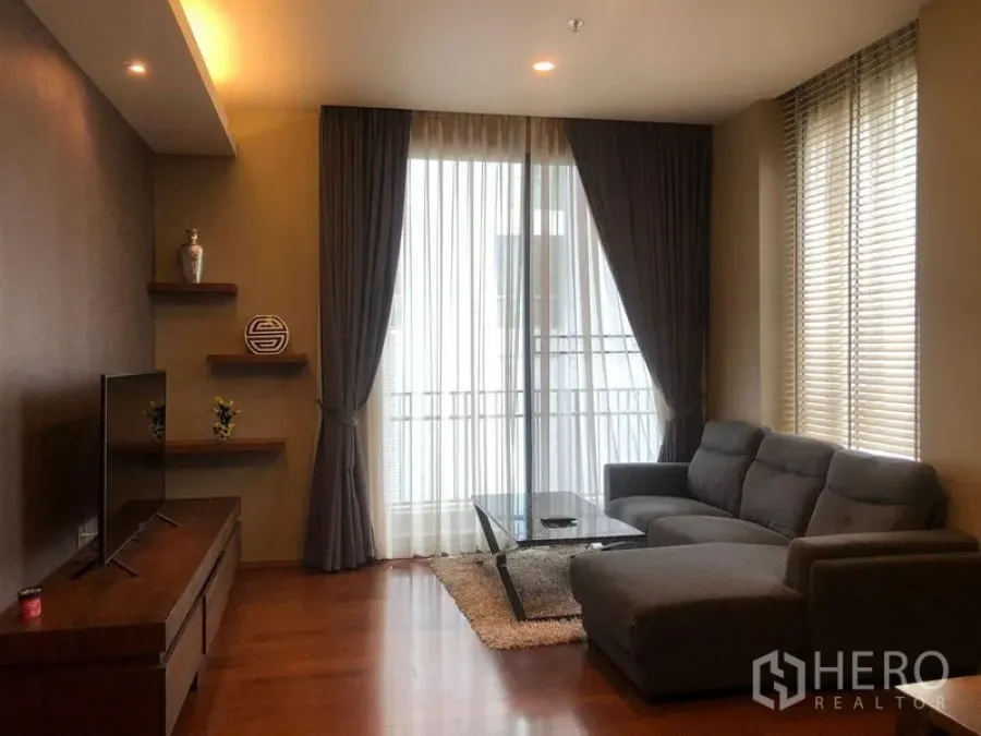 公寓 出租或出售在Watthana, Bangkok - 明亮客厅，落地推拉门通阳台，转角沙发与电视柜。
