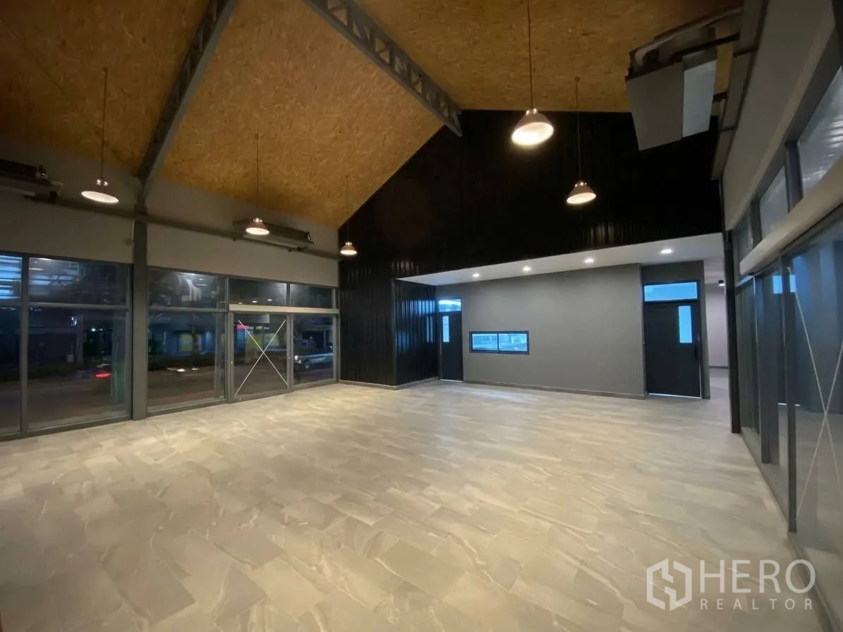 พื้นที่ขายของ for rent in Khlong Toei, Bangkok - ภายในสไตล์โชว์รูม เพดานจั่วสูง ไฟแขวน และผนังกระจกบานใหญ่เห็นทิวทัศน์ถนนยามค่ำ