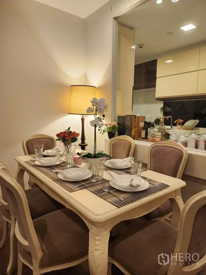 Condominium for rent in Phra Khanong, Bangkok - Close-up of classic dining table with place settings, lamp, and pass-through to the kitchen.