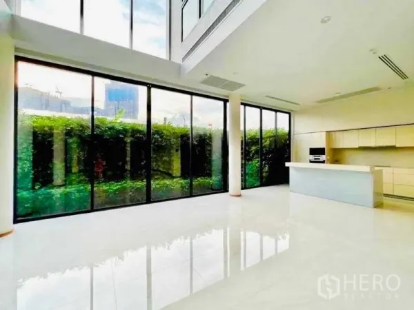 独立式住宅 出售在Huai Khwang, Bangkok - 挑高客厅配落地玻璃与现代中岛厨房，面向绿篱花园，采光充足。
