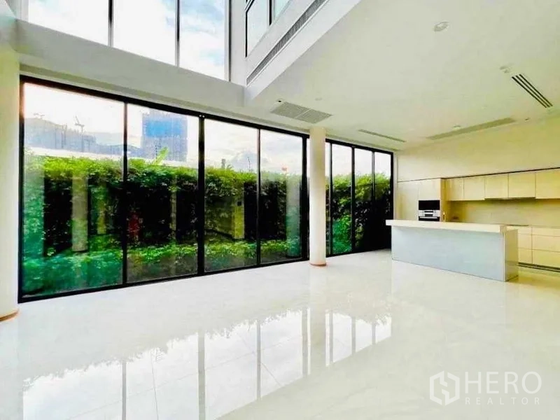 独立式住宅 出售在Huai Khwang, Bangkok - 挑高客厅配落地玻璃与现代中岛厨房，面向绿篱花园，采光充足。