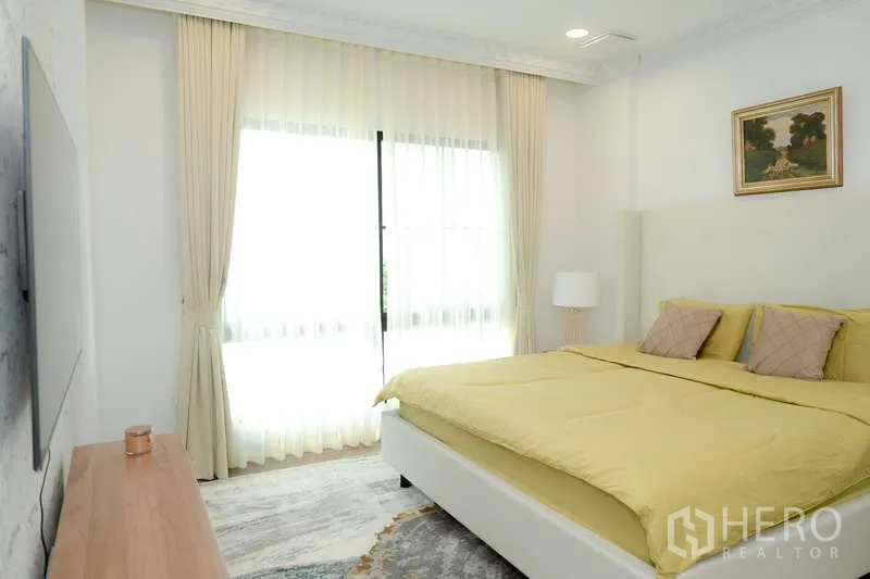 Detached House for rent or sale in Saphan Sung, Bangkok - Bedroom with balcony-style sliding doors, sheer curtains and a TV wall.