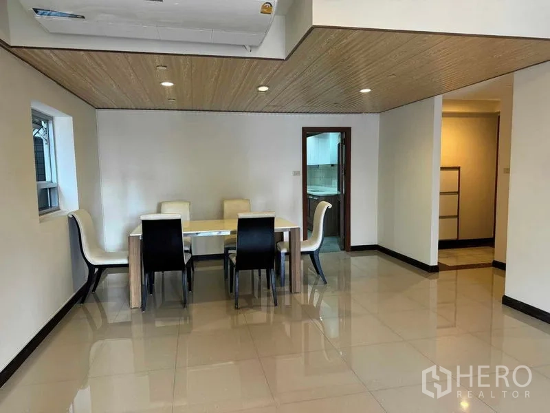 公寓 出租在Pathum Wan, Bangkok - 明亮的餐区，六人餐桌，亮面瓷砖与木纹天花，旁有通往厨房的门。