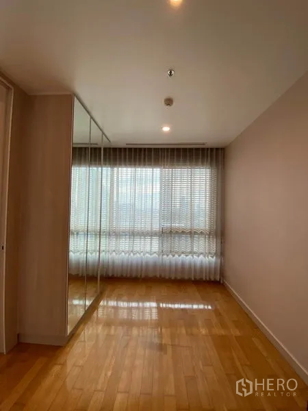 Condominium for rent or sale in Yan Nawa, Bangkok - Empty bedroom with mirrored wardrobe, light wood flooring and sheer curtains over a wide window.