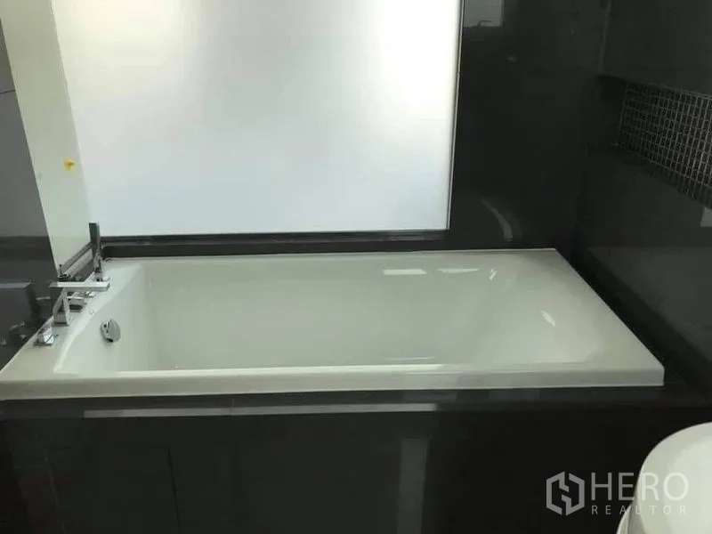 Condominium for rent or sale in Phaya Thai, Bangkok - Built-in rectangular bathtub with black tile surround and frosted window.