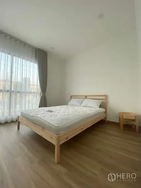 Townhouse for rent in Bang Kapi, Bangkok - Airy second bedroom with wooden bed frame, floor-to-ceiling window and light wood flooring.