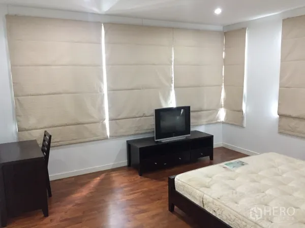 Condominium for rent in Khlong Toei, Bangkok - Bright bedroom with wood floors, a work desk, TV console, and large windows with beige blinds.