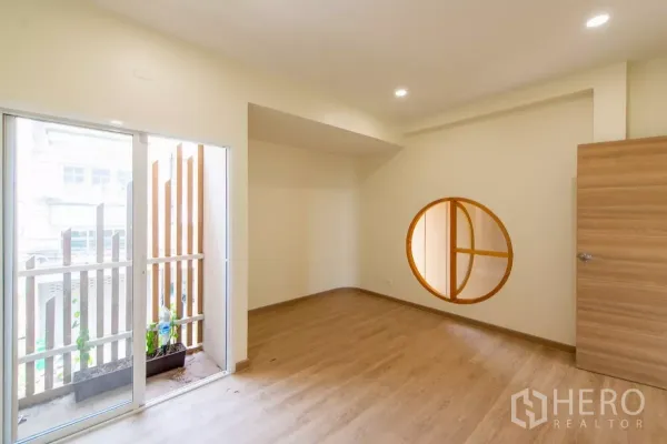 Townhouse for sale in Lat Phrao, Bangkok - Spacious room with sliding glass door to a small balcony and a round feature window.