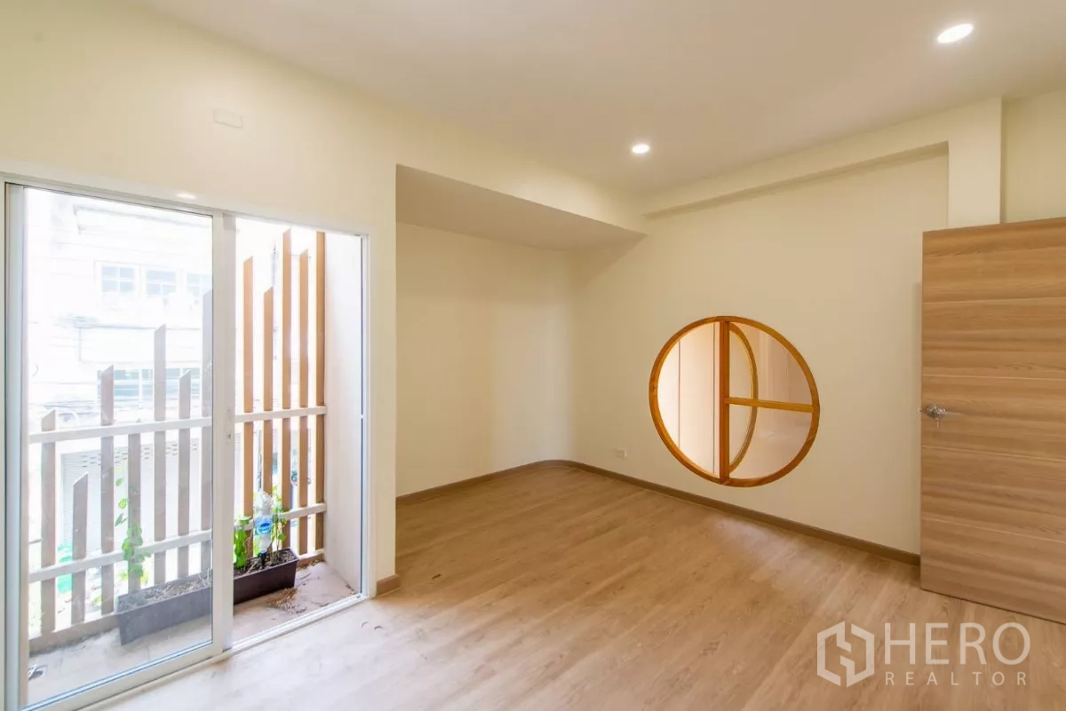 Townhouse for sale in Lat Phrao, Bangkok - Spacious room with sliding glass door to a small balcony and a round feature window.