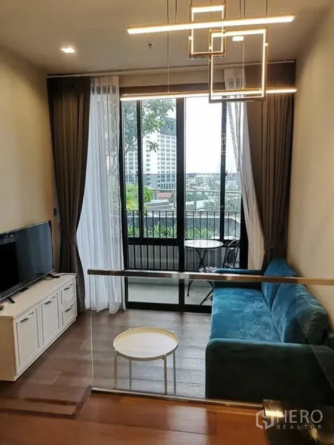 公寓 出租在Ratchathewi, Bangkok - 温馨客厅，蓝绿色沙发、几何吊灯与电视柜，连接阳台，城市景观，近胜利纪念碑。
