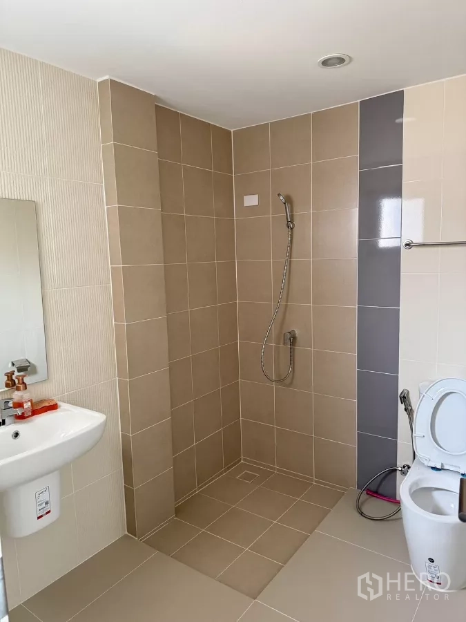 Detached House for rent in Saphan Sung, Bangkok - Spacious bathroom with walk-in shower, beige tiles, toilet and wall-mounted sink.