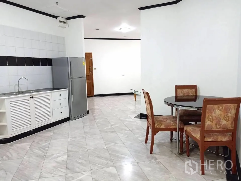 Condominium for rent in Watthana, Bangkok - Open-plan kitchen with white cabinets, stainless sink, fridge, and round dining table.