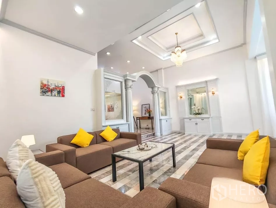 Detached House for rent in Yan Nawa, Bangkok - Elegant living room featuring classical columns, coffered ceiling, and brown sofas with yellow cushions.