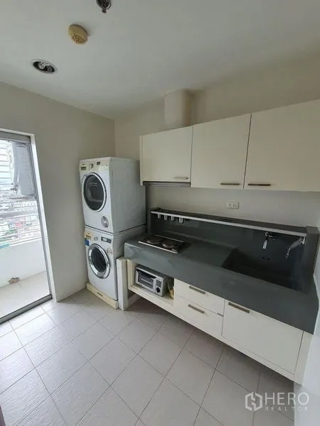 Condominium for sale - Separate kitchen with cabinetry, cooktop, and stacked washer and dryer beside a service balcony.