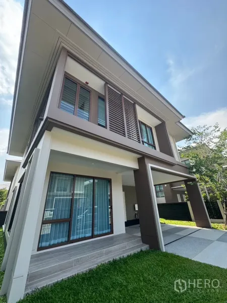 Detached House for rent or sale in Bang Kapi, Bangkok - Angled facade view showing louvered upper windows, covered porch and carport beside a neat lawn.
