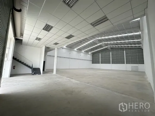工厂 出租在Pathum Thani - 仓库内部视角，钢结构屋顶、装卸卷门与楼梯。