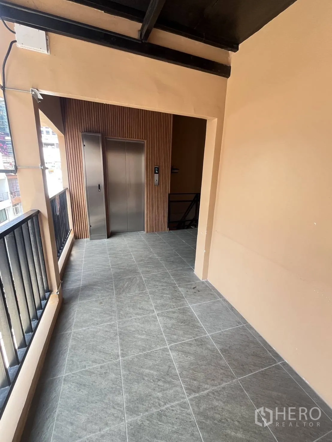 零售空间 for rent in Watthana, Bangkok - 带黑色栏杆的瓷砖走廊尽头为电梯大堂。