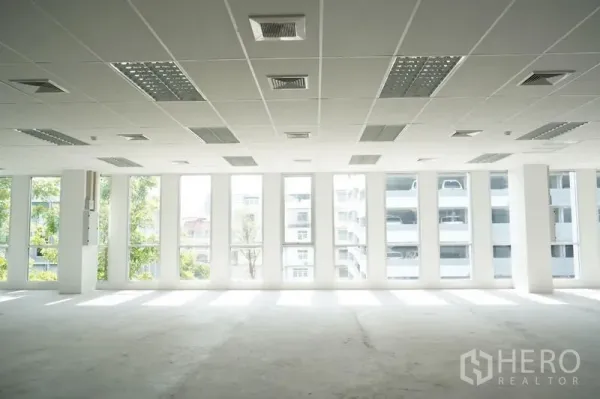 Office Space for rent in Bang Na, Bangkok - Bright empty office interior with tall windows, suspended ceiling, lighting panels and AC vents in an open-plan layout.