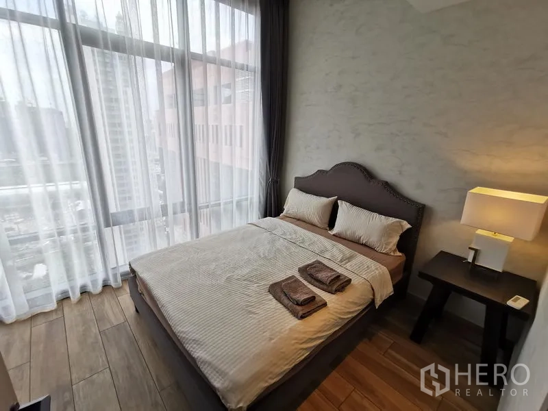 公寓 出租在Watthana, Bangkok - 次卧舒适，配双人床、床头灯与轻薄窗帘，通过高窗可见城市景致。