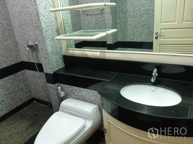 Condominium for rent in Khlong Toei, Bangkok - Bathroom with wide mirror, black granite countertop, toilet and shower area.