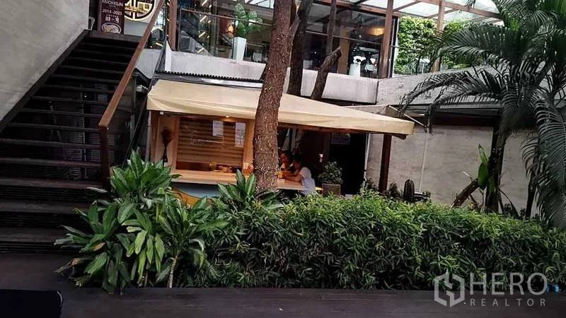 零售空间 出租在Watthana, Bangkok - 中庭内的绿色小铺带遮阳篷，环植绿化与宽阔楼梯。