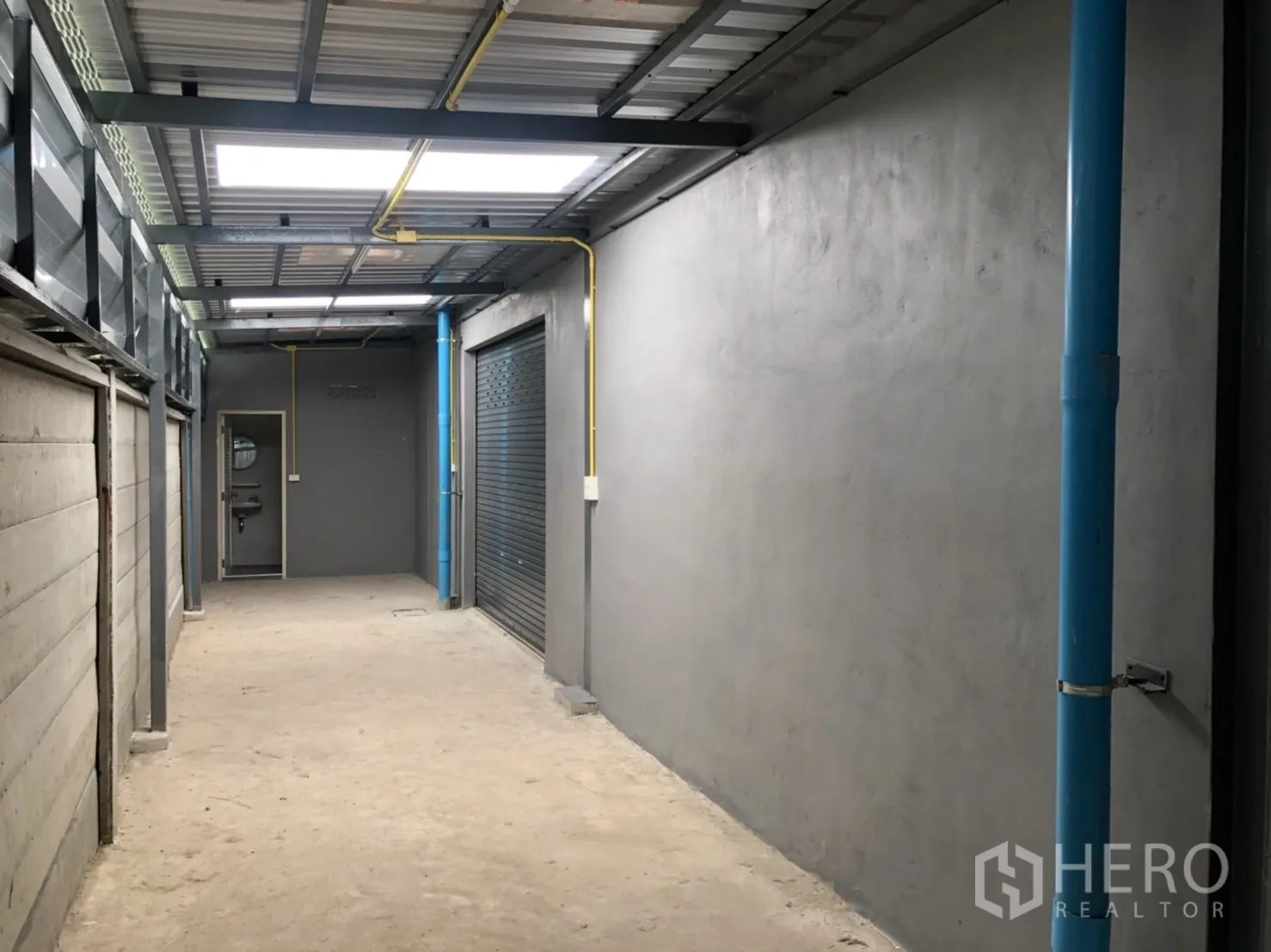 Warehouse for rent in Lam Luk Ka, Pathum Thani - Covered service corridor with blue plumbing and yellow conduit leading to utility rooms.