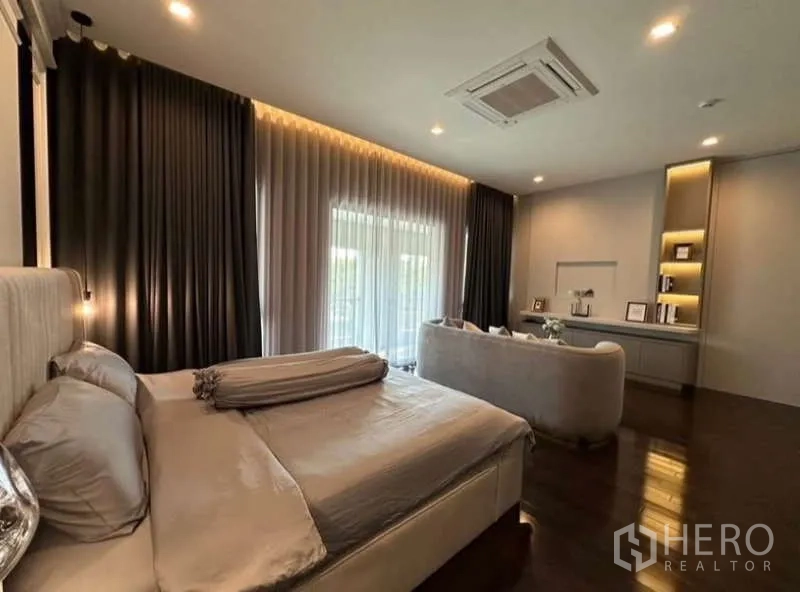 独立式住宅 出租在Lat Krabang, Bangkok - 套房卧室，带沙发休息区、展示柜与通往阳台的纱帘。