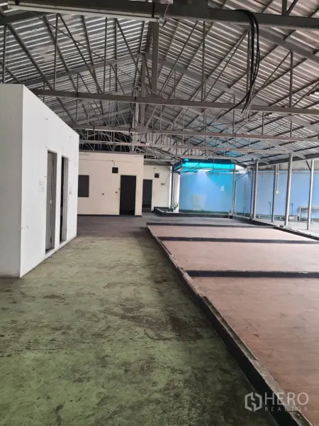 Shophouse for rent in Khlong Toei, Bangkok - Open-plan shophouse interior with high metal truss roof, concrete floors, raised platforms and service rooms.