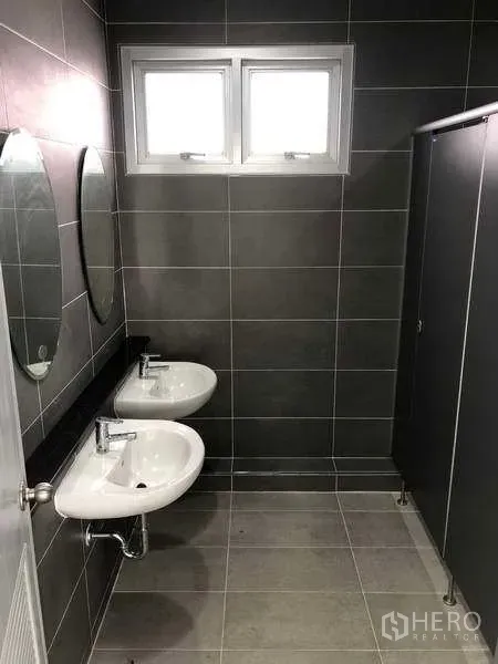Factory for rent in Bang Sao Thong, Samut Prakan - Clean tiled restroom with twin sinks, mirrors and a private cubicle.