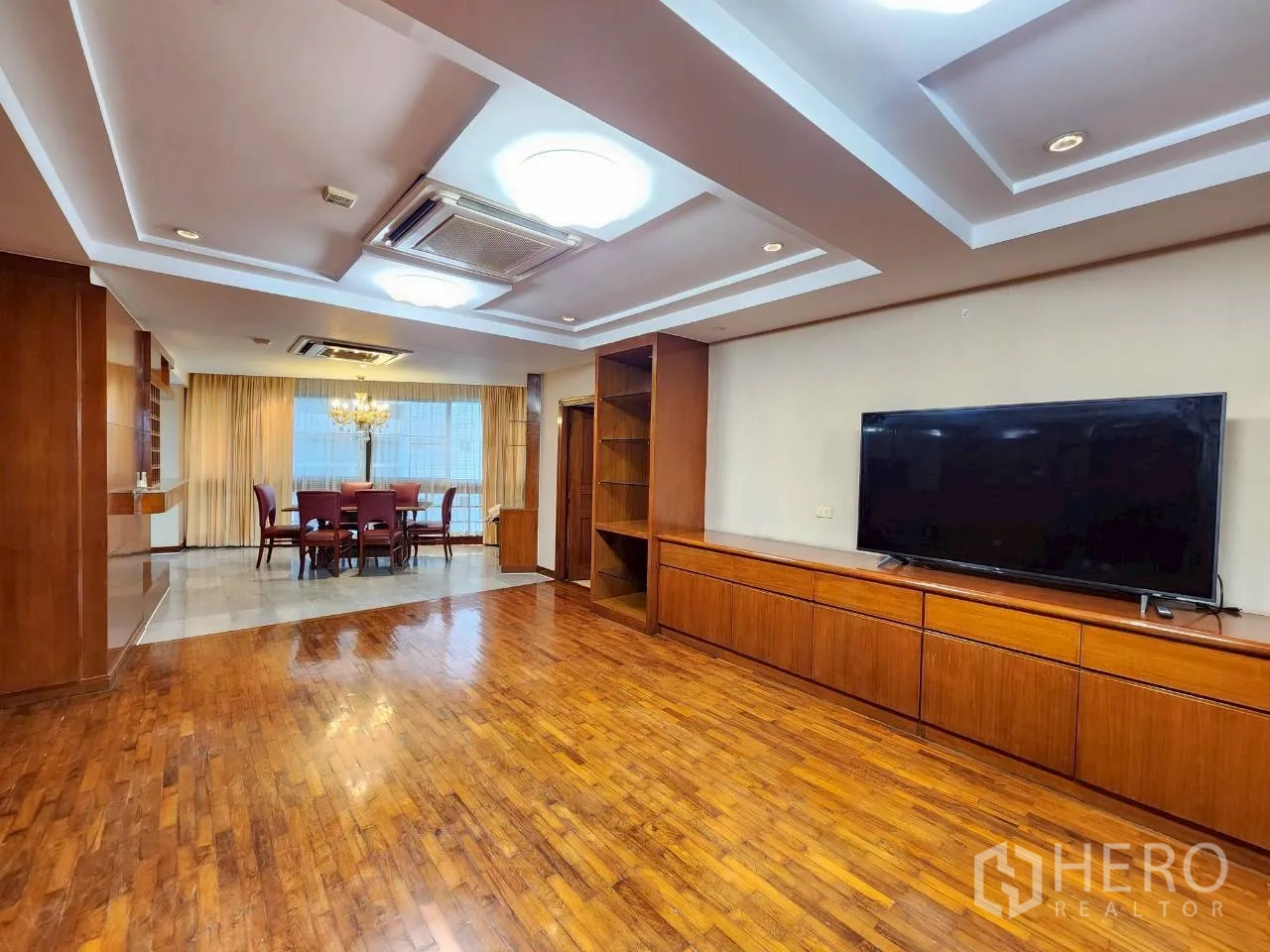 Condominium for rent in Khlong Toei, Bangkok - Living room flowing to the dining zone with chandelier, curtains and expansive hardwood floors.