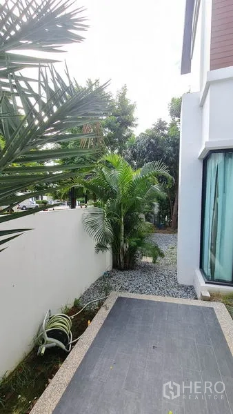 Detached House for sale in Samut Prakan - Small side garden with palms, gravel path and a tiled patio along the house.