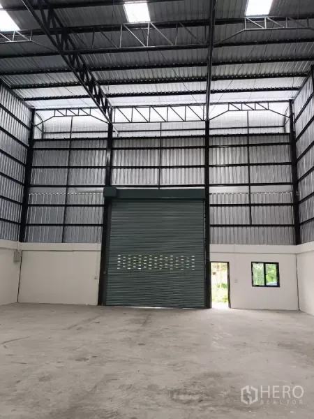 Warehouse for rent in Bang Phli, Samut Prakan - Open warehouse floor facing an oversized roller shutter and side entry door with natural light.