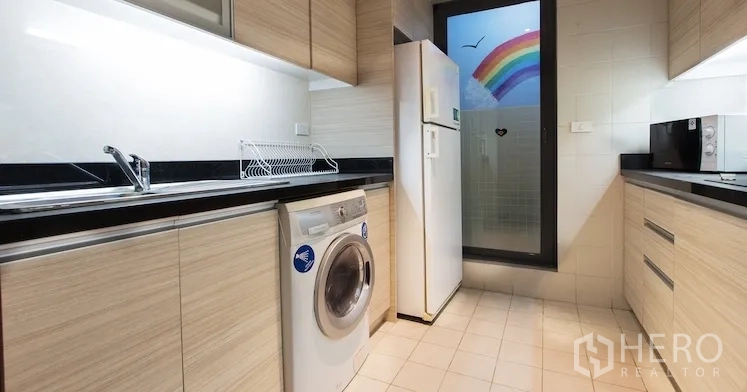 Condominium for rent in Sathon, Bangkok - Enclosed kitchen with light-wood cabinets, black countertops, refrigerator and washing machine.