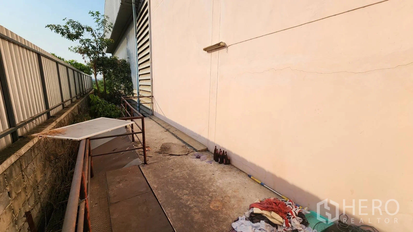 Warehouse for rent in Nonthaburi - Side yard with concrete path and maintenance items against the wall.