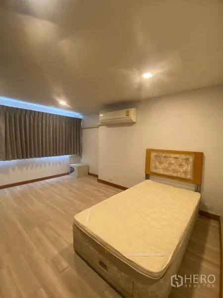 Condominium for rent in Sathon, Bangkok - Spacious bedroom with bed, wood-look flooring, air conditioner, and blackout curtains along one wall.