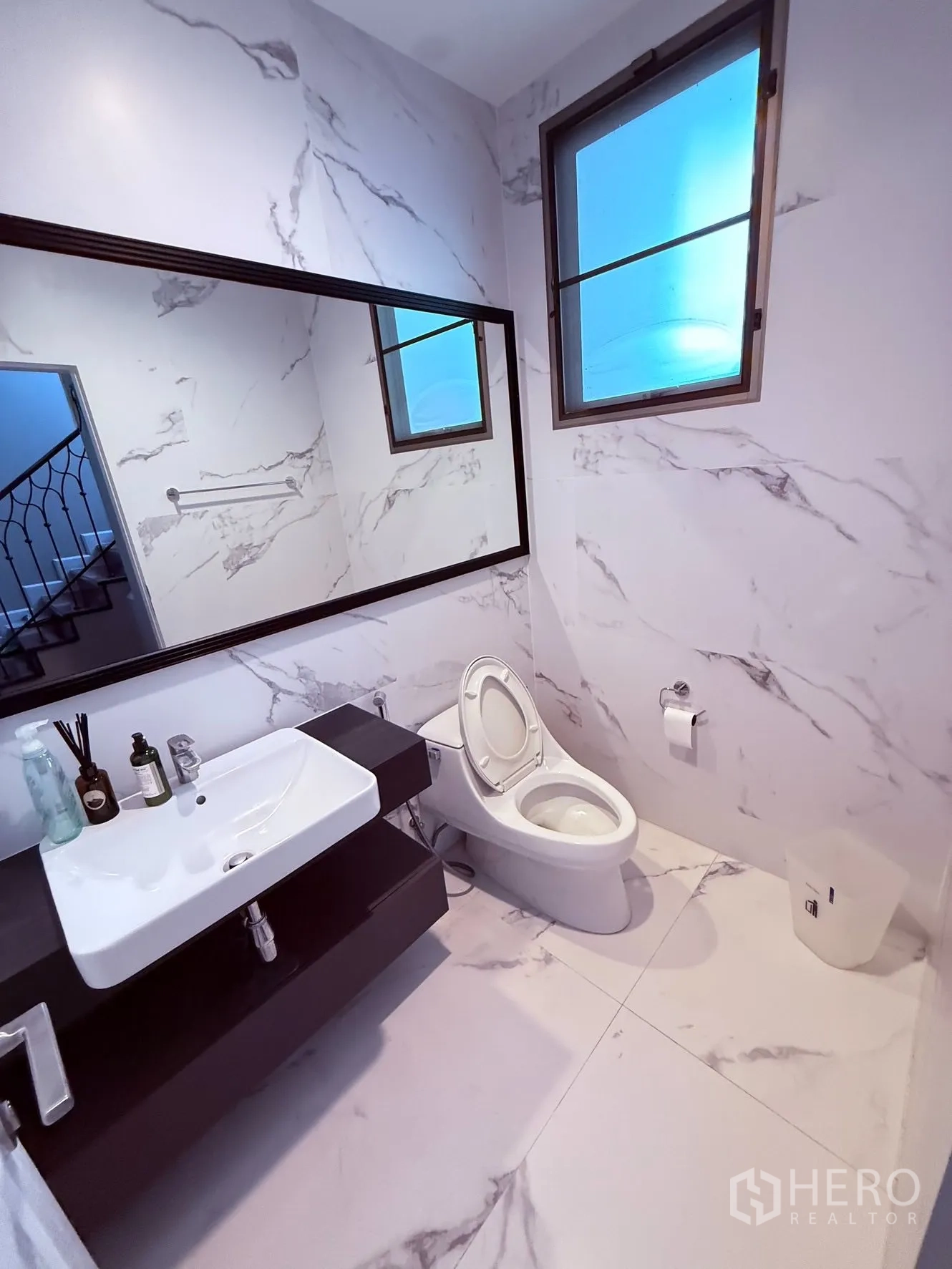 Detached House for rent or sale in Prawet, Bangkok - Bathroom with marble-effect tiles, large mirror, vanity sink, toilet, and window.
