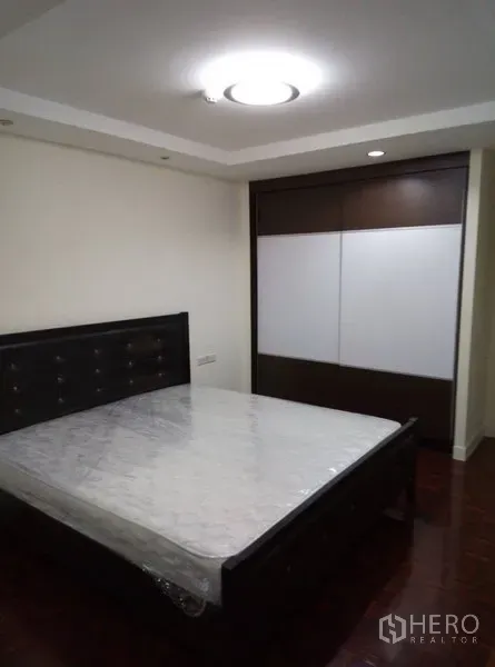Condominium for rent in Watthana, Bangkok - Primary bedroom with large bed, sliding wardrobe, and ceiling light in neutral tones.