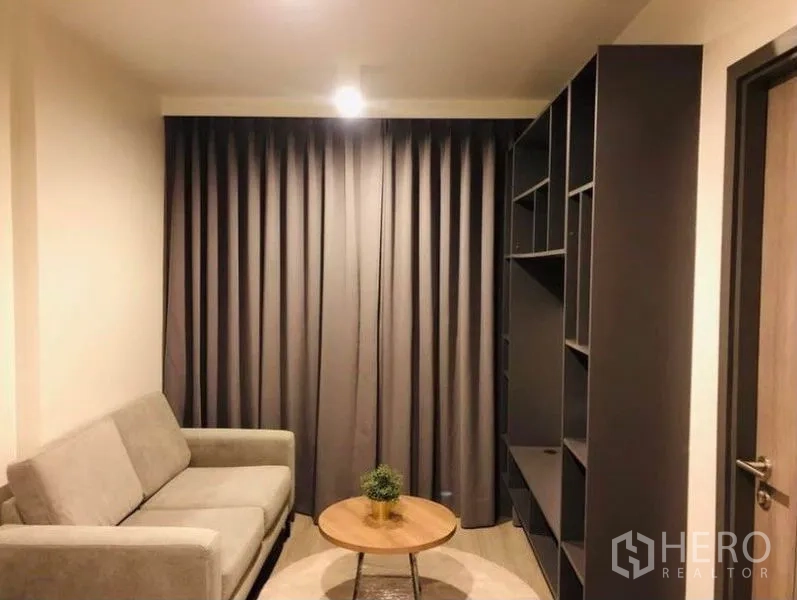 Condominium for rent or sale in Pathum Wan, Bangkok - Cozy living room with grey curtains, sofa, built-in shelving and a round coffee table.