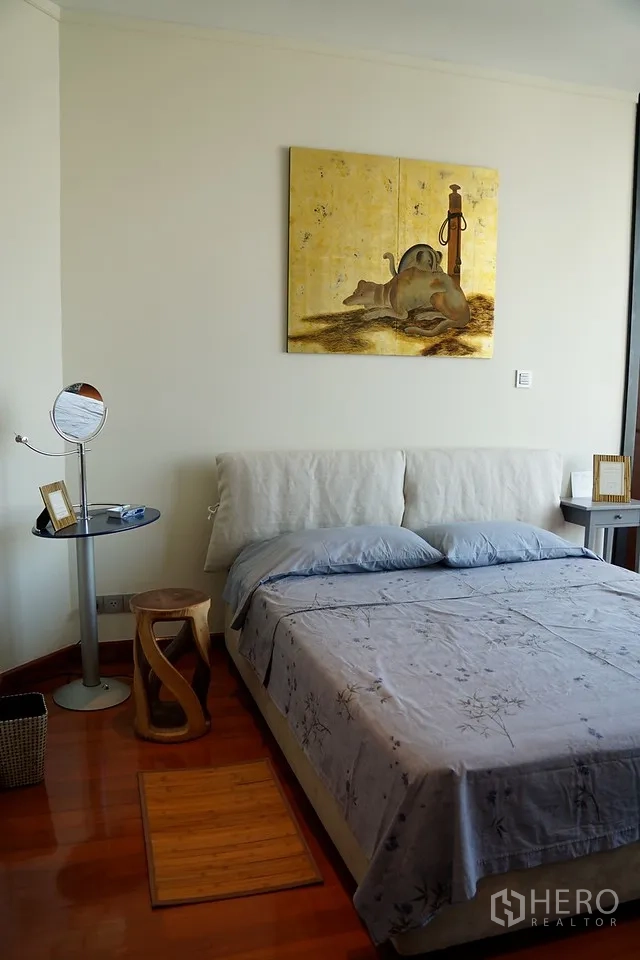 Condominium for rent in Bang Rak, Bangkok - Cozy bedroom with artwork above an upholstered headboard and warm wood flooring.