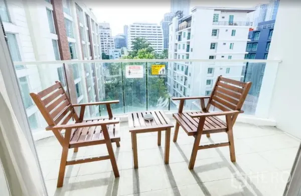 Condominium for rent in Khlong Toei, Bangkok - Balcony with two wooden chairs and a small table overlooking low-rise buildings and greenery.
