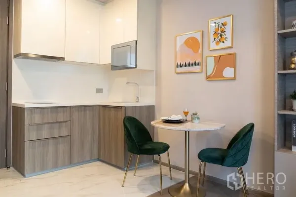 Condominium for rent in Watthana, Bangkok - Compact L-shaped kitchenette and two-seat dining nook with modern wall art.