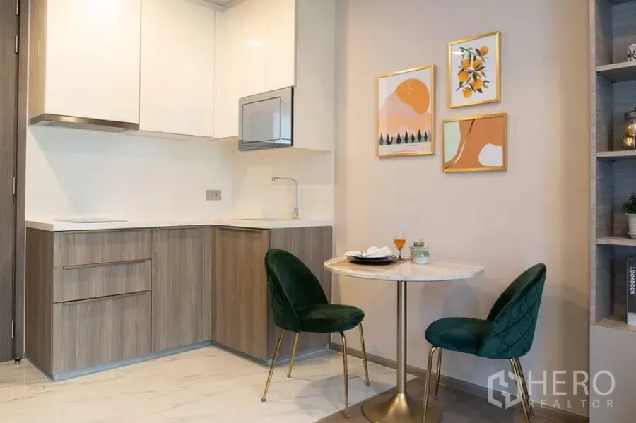 Condominium for rent in Watthana, Bangkok - Compact L-shaped kitchenette and two-seat dining nook with modern wall art.
