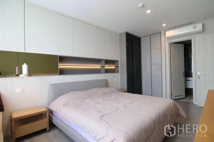 Condominium for rent in Bang Sue, Bangkok - Bright master bedroom with built-in headboard shelving, large wardrobes, and door to adjacent bathroom.
