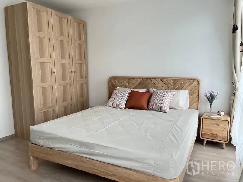 Townhouse for rent in Prawet, Bangkok - Master bedroom featuring a large bed, wood wardrobe, bedside table, and natural light.