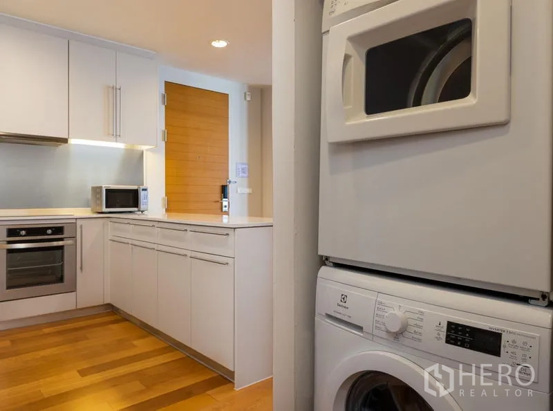 Condominium for rent in Bang Kho Laem, Bangkok - Compact kitchen entry with stacked washer and dryer next to cabinetry and wooden door.