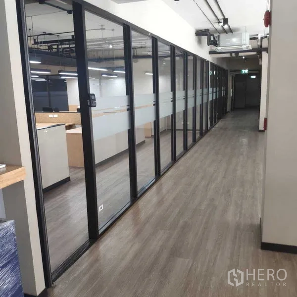 Office Space for rent - Hallway with full-height glass partitions and wood-look flooring beside work areas.