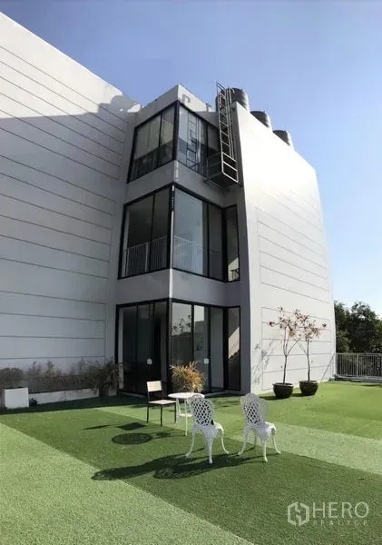 零售空间 出租在Bang Kapi, Bangkok - 现代白色低层建筑外立面，巨窗面向景观化屋顶草坪与户外座椅