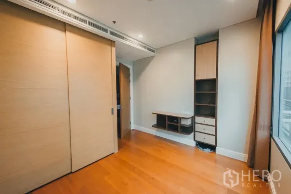 Condominium for rent in Khlong Toei, Bangkok - Secondary bedroom or study with sliding wardrobe, built-in shelves and desk, wood flooring and window.