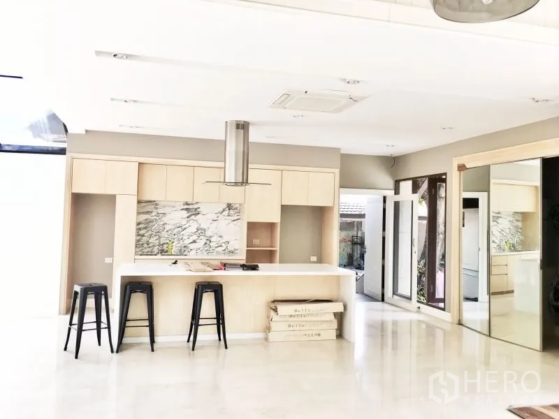 Detached House for rent in Khlong Toei, Bangkok - Bright modern kitchen with marble backsplash, island counter and stools, opening to glass doors.